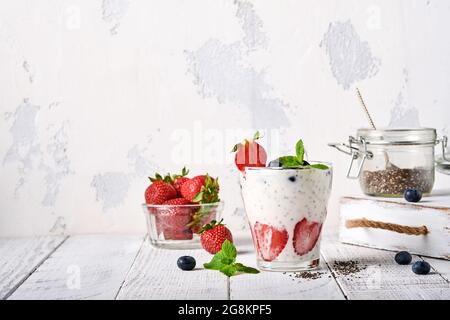 Zwei Chia-Erdbeerkerne mit Smoothie oder Milchshake mit Erdbeer- und Blaubeerminze in Glas auf hellgrauem Hintergrund. Sommer und gesunde Dieti Stockfoto