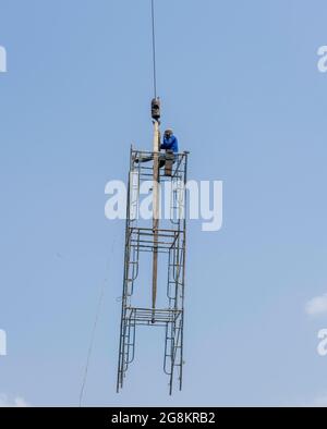 Mobiler Kran, der einen Mann, der auf der provisorischen Struktur sitzt, in die Luft hebt Stockfoto