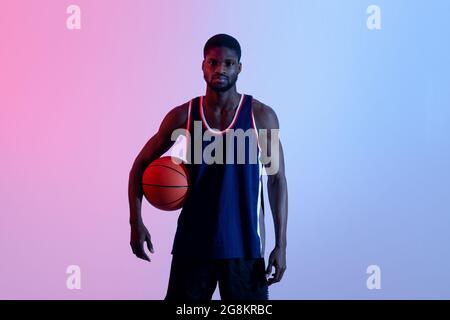 Porträt eines motivierten schwarzen Basketballspielers, der den Ball in Neonbeleuchtung hält Stockfoto