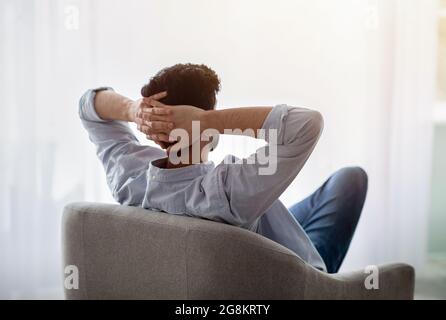 Fauler Tag. Entspannter Kerl, der sich auf einem bequemen Sessel ausruht, die Hände hinter dem Kopf hält und die Stille und den freien Platz genießt Stockfoto