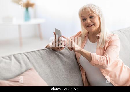 Lächelnde reife Frau, die ein Mobiltelefon auf dem Sofa benutzt Stockfoto