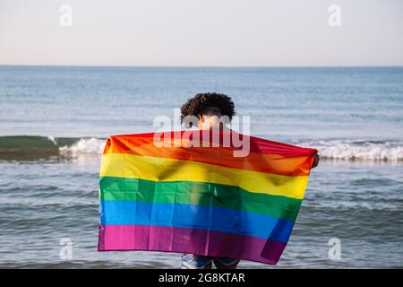 Junger latein mit lgtbi-Flagge am Strand Stockfoto