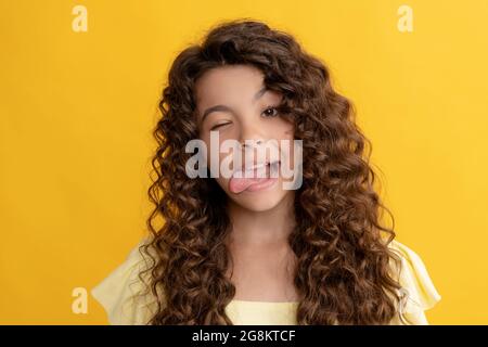 Lustiges Kind mit langen lockigen Haaren und perfekter Haut zeigt Zunge, Mode Stockfoto