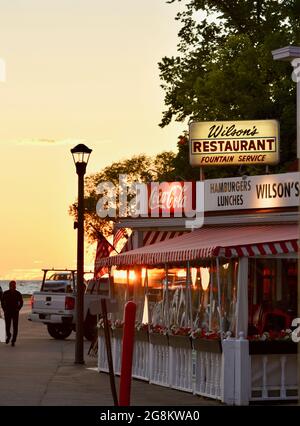 Herrlicher goldener Sonnenuntergang, der im Gelände reflektiert wird, mit Touristen, die zu Wilson's Ice Cream Parlor, gegründet 1906, Ephraim, Door County, Wisconsin, USA Stockfoto