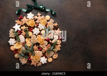 Kreative Weihnachtskugel mit verschiedenen Keksen, Zimt, Anissternen, Beeren, Orangenchips, Fichtenzweige auf braunem Hintergrund. Neujahrskarte Stockfoto