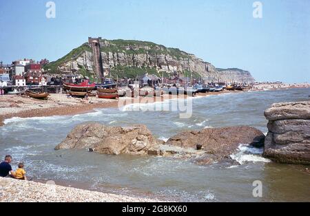 1975, ein Blick aus dieser Ära der festgetäuten Fischerboote auf dem Stade, einem Kiesstrand in Hastings, East Sussex, England, Großbritannien. Im Zusammenhang mit der berühmten Schlacht von Hastings im Jahr 1066 wurde die Stadt im 19. Jahrhundert zu einem beliebten Badeort. Die Fischerei war für Hastings, das die größte Strandfischerflotte Großbritanniens besaß, schon immer von wirtschaftlicher Bedeutung. In der Ferne die East Hill Cliff Railway oder East Hill Lift, eine Standseilbahn auf der steilen Felswand. Eröffnet im Jahr 1902 und mit Blick auf das Stade, zu dieser Zeit wurde es zu einem elektrischen Betrieb modernisiert. Stockfoto