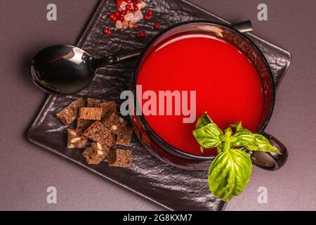 Traditionelle Tomatensuppe in einer Tasse. Basilikum, Croutons, Gewürze, Besteck. Schwarzer Stein Beton Hintergrund, minimalistisches Design, Draufsicht Stockfoto