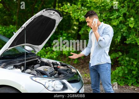 Verwirrter Fahrer, der unter die Motorhaube schaute und den Autoservice anrief Stockfoto