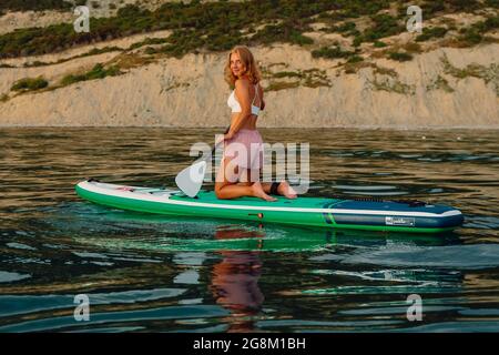 25. Juni 2021. Anapa, Russland. Schlanke Mädchen auf Stand-up-Paddle-Board auf ruhiger See. Frauen sitzen auf dem Red Paddle SUP-Board im Meer. Stockfoto