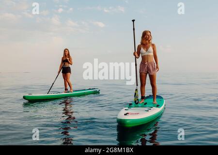 25. Juni 2021. Anapa, Russland. Sportliche Mädchen schweben auf dem Stand Up Paddle Board auf ruhiger See. Frauen auf dem Red Paddle SUP-Board im Meer. Stockfoto