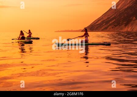 25. Juni 2021. Anapa, Russland. Frauen auf Red Paddle stehen am ruhigen Meer mit Sonnenuntergang oder Sonnenaufgang auf dem Paddle Board. Stockfoto