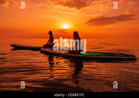 25. Juni 2021. Anapa, Russland. Frauen auf Red Paddle stehen am ruhigen Meer mit Sonnenuntergang oder Sonnenaufgang auf dem Paddle Board. Stockfoto