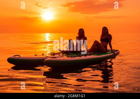 25. Juni 2021. Anapa, Russland. Frauen auf Red Paddle stehen am ruhigen Meer mit Sonnenuntergang oder Sonnenaufgang auf dem Paddle Board. Stockfoto