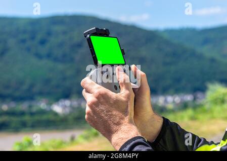 Der Mann hält eine Drohnenfernbedienung mit einem Smartphone mit grünem Bildschirm, das mit ihm verbunden ist. Stockfoto
