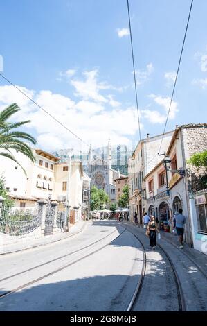 Soller, Spanien - 19. Juni 2021: Straße mit den Straßenbahnschienen und der Dorfkirche im Hintergrund Stockfoto