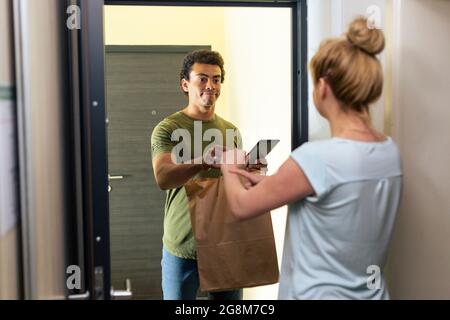 Ein Mann, der Lebensmittel geliefert hat, vor der offenen Tür der Wohnung, in einer Situation, in der er sich gegenüber einer Frau rechtfertigt, die ein Paket erhielt, das lat war Stockfoto