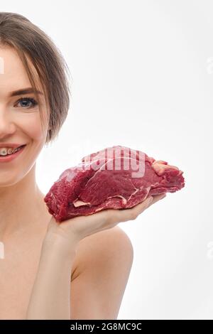 Junge Frau hält rohes Rinderfleisch auf der Handfläche (halb Stück weibliches Gesicht) Stockfoto