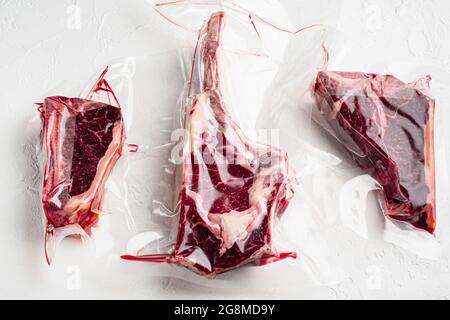 Trockenes, gereiftes Steak im Vakuum. Fleischprodukte in Plastikpackung, Tomahawk, T-Knochen und Club Steak Schnitte, auf weißem Stein Hintergrund Stockfoto