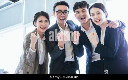 Junge vietnamesische Geschäftsteams in Anzügen mit erhobenen Fäusten im Büro Stockfoto