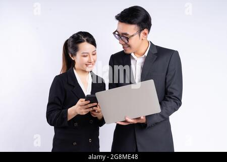 Junge vietnamesische Mitarbeiter arbeiten in Anzügen am Laptop vor einer Wand Stockfoto