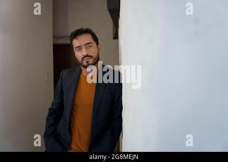 Gutaussehender bärtiger hispanischer Mann mit einem Blazer, der sich mit einem ernsthaften Gesichtsausdruck an der Wand lehnt Stockfoto