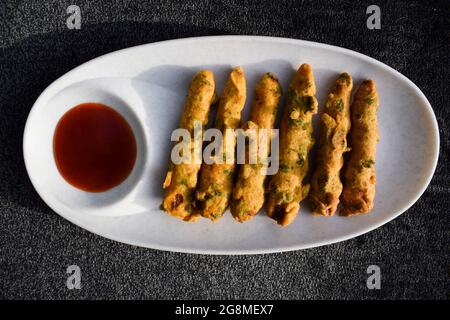 Knusprige Babykorn-Fritten, serviert mit Tomatenketchup auf weißem Teller. Köstliche frittierte Pakoda-Snacks aus Babykorn Stockfoto