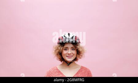 Schönes junges Mädchen trägt einen Fahrradhelm lächelnd und posiert für die Kamera. Das Mädchen ist in einem lässigen rosafarbenen Oberteil gekleidet. Isoliert auf rosafarbenem Hintergrund aufgenommen im Studio. Stockfoto
