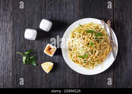 Sommer-Spaghetti alla carrettiera mit Minzblättern, Zitronenschale, Pecorino-Käse, Chilischoten-Flocken, Petersilie und geriebenen Zucchini auf einem weißen Teller Stockfoto