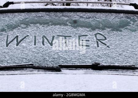 Das Wort WINTER steht auf der Windschutzscheibe eines Autos. Erster Schnee. Stockfoto