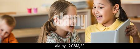 Fröhliche interracial Mädchen Blick auf Buch in der Nähe Junge auf verschwommenem Hintergrund, Banner Stockfoto