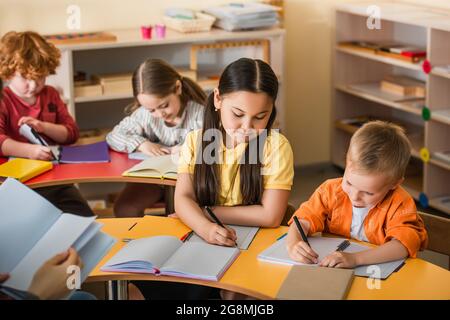 Multiethnische Kinder schreiben in Notizbüchern während des Unterrichts in der montessori-Schule Stockfoto