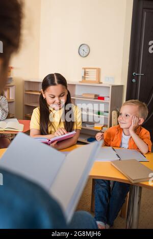 asiatische Mädchen Buch in der Nähe Junge und verschwommen Lehrer im Klassenzimmer zu lesen Stockfoto