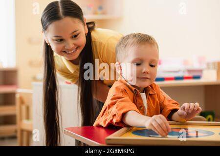 Lächelndes asiatisches Mädchen, das Jungen ansieht, der in der montessori-Schule Kartenerde kombiniert Stockfoto