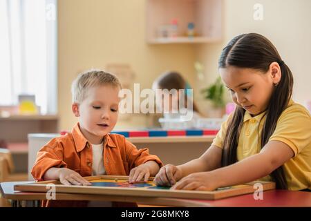 Multiethnische Kinder kombinieren Weltkarte Puzzle in der Nähe Mädchen auf verschwommenem Hintergrund Stockfoto