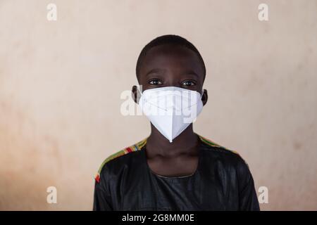 Ehrliche Fotografie eines kleinen afrikanischen Jungen, der im Freien in Bamako, Mali, steht. Dieser Junge trägt eine Gesichtsmaske, um sich vor dem Coronavir zu schützen Stockfoto