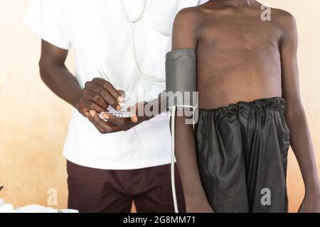 Dies ist ein Bild eines afrikanischen Arztes oder einer Krankenschwester, die den Blutdruck an einem kleinen schwarzen Kind misst. Der Salzverbrauch in Afrika ist in die Höhe geschossen Stockfoto