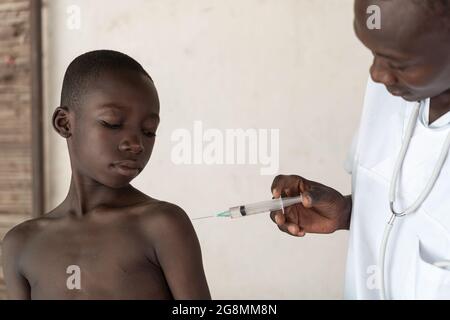 Junger afrikanischer schwarzer Junge bekommt Impfstoff in die Schulter geschossen. Die Pandemie verursachte viele Todesfälle. Ein Impfstoff hilft, die Ausbreitung der Krankheit zu verhindern. Stockfoto