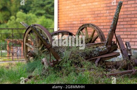 Vor dem Hintergrund eines Backsteinhauses ein alter gebrochener Holzwagen mit gebrochenen Rädern aus Holz Stockfoto