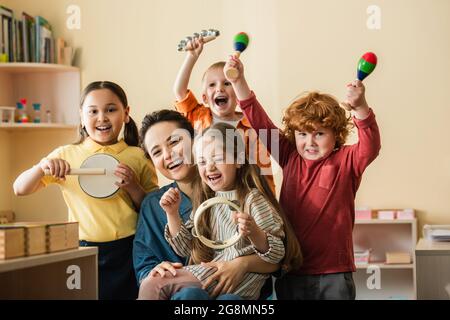 Aufgeregte multiethnische Kinder spielen Musikinstrumente in der Nähe glücklicher Lehrer Stockfoto