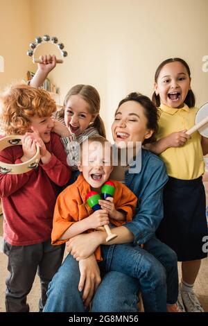 Aufgeregter Lehrer lacht, während multiethnische Kinder Musikinstrumente spielen Stockfoto