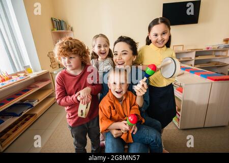 Glücklicher Lehrer mit interrassischen Kindern, die in der montessori-Schule Musikinstrumente spielen Stockfoto