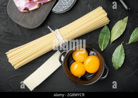 Traditionelle Italienische Pasta Carbonara Zutaten. Speck, Spaghetti, Parmesan und Pecorino-Käse, Ei, Knoblauch, auf schwarzem Stein Hintergrund, Draufsicht Stockfoto
