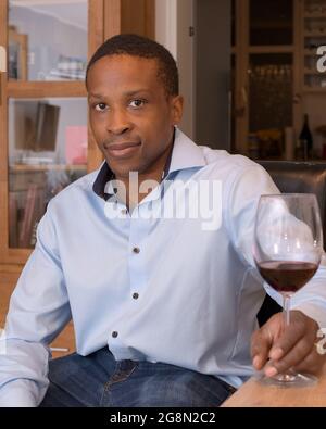Junger Mann mit blauem Hemd, der sich zu Hause bei einem Glas Rotwein entspannt. Stockfoto