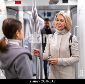 Zwei weibliche Fahrgäste, die auf dem Weg zur Arbeit in einem U-Bahn-Auto sprechen Stockfoto