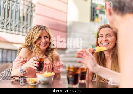Frau mittleren Alters, die beim Plaudern mit ihren Freunden einen Drink hält Stockfoto