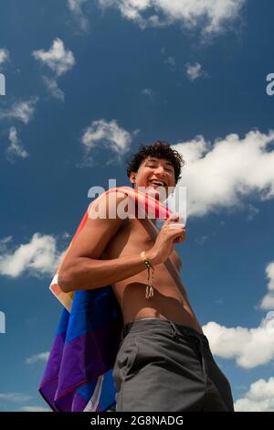 Porträt eines jungen schwulen hispanischen Jungen, der die Kamera anschaut und die LGBT-Flagge hält – Fokus auf vertikales Bild im Gesicht Stockfoto