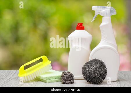 Plastikflaschen mit Spülmittel, Glas- und Fliesenreiniger, eine Bürste, Schwämme auf dem grünen natürlichen Hintergrund. Wasch- und Reinigungskonzept. Stockfoto