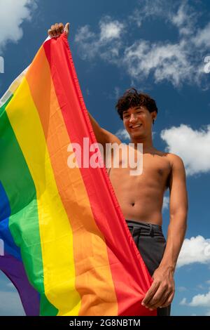 Porträt eines jungen schwulen hispanischen Jungen, der die Kamera anschaut und die LGBT-Flagge hält – Fokus auf vertikales Bild im Gesicht Stockfoto