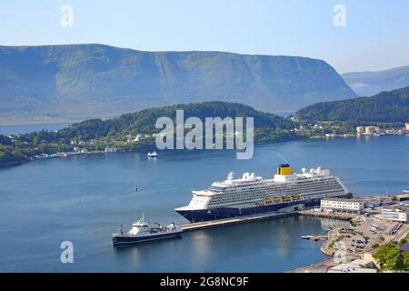 Das Kreuzschiff mit blauem Rumpf und gelbem Trichter dockte im Hafen von Alesund, Norwegen, an. Schöne Fjordlandschaft mit Berg im Hintergrund Stockfoto