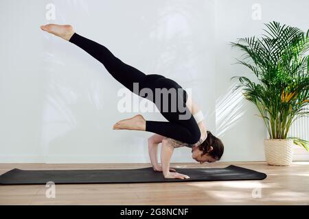 Meisterhafte qualifizierte Frau mit Schulter-Tattoo üben advansed Yoga-Handstände in einem großen Studio. Seitenansicht Stockfoto